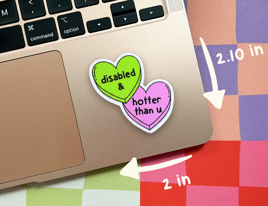 Two heart-shaped stickers on a laptop trackpad, one green reading 'disabled &' and one pink reading 'hotter than u', with white arrows and text indicating dimensions 2.10 in by 2 in.