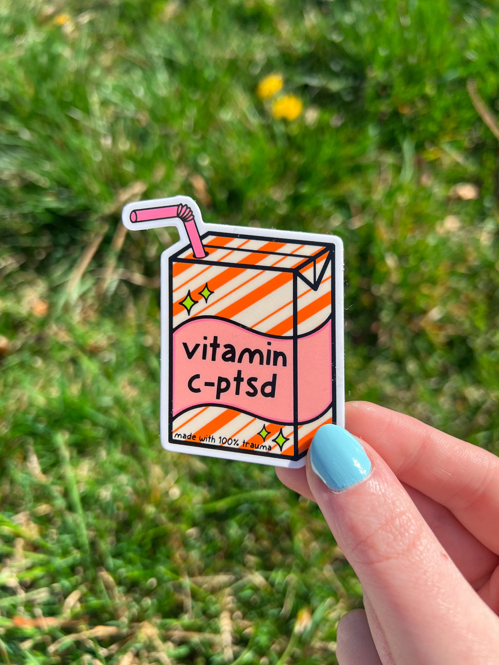 A sticker in the shape of a juice box with the words "vitamin c-ptsd" in black text. The juice box is pink with orange and white stripes. The sticker has a pink straw and the text "made with 100% trauma".