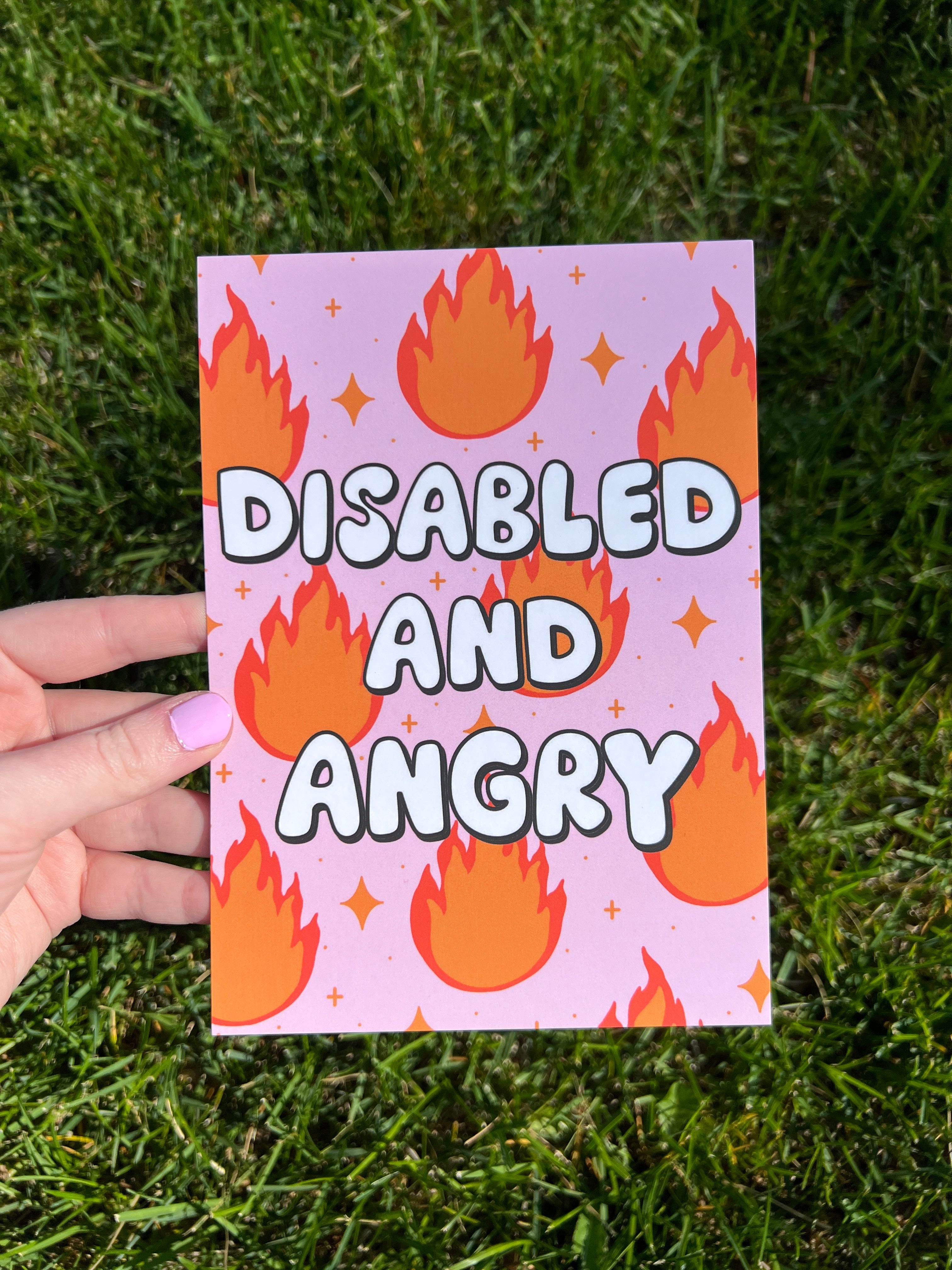 A rectangular print with a light pink background featuring a repeating pattern of orange and red flames and small yellow four-pointed stars. The text "DISABLED AND ANGRY" is printed in large, bold, white letters with a thick black outline.