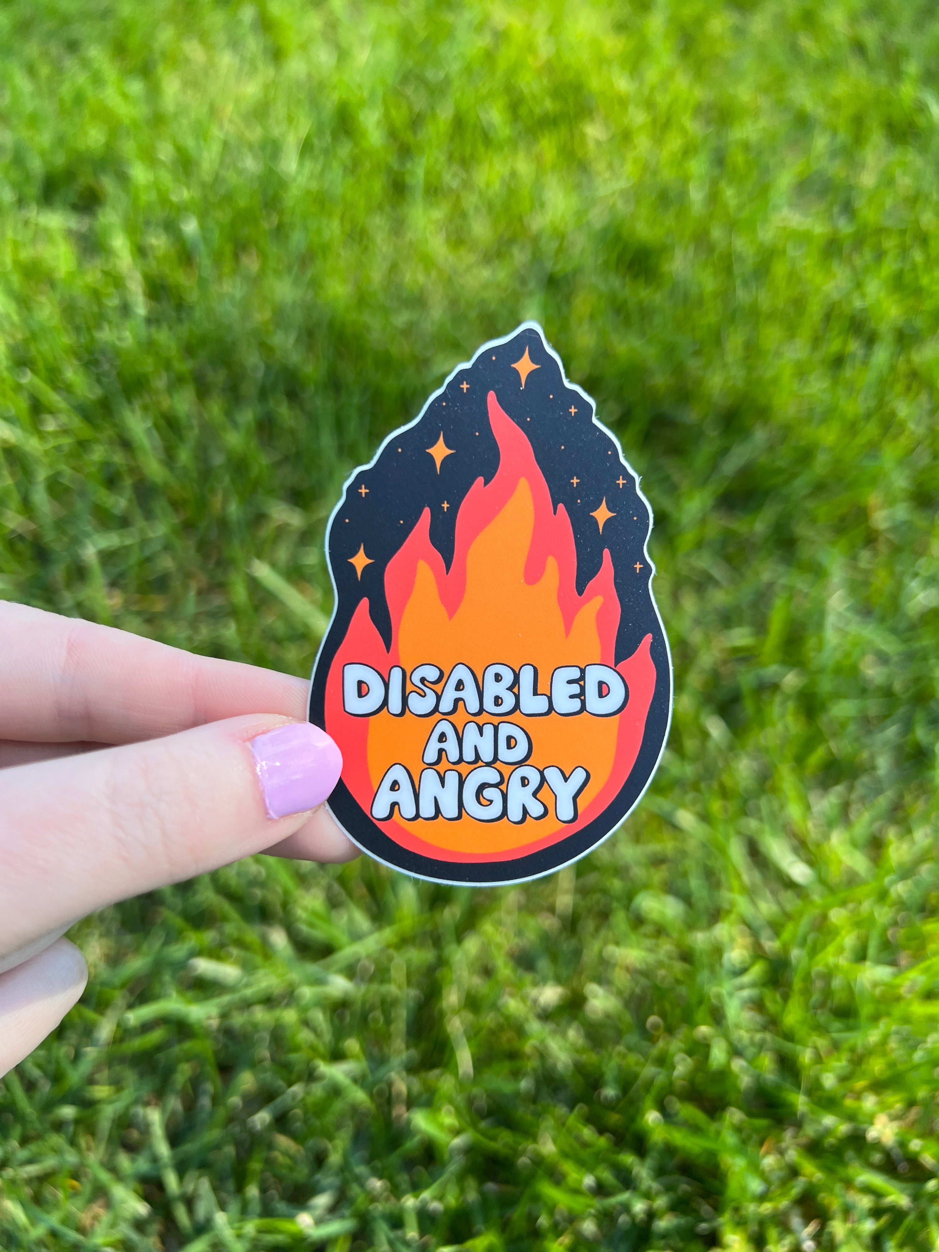 A die-cut sticker featuring a stylized flame graphic in shades of orange and red against a dark background with small star accents. The text "DISABLED AND ANGRY" is printed in a bold, white, rounded font across the center of the flame.