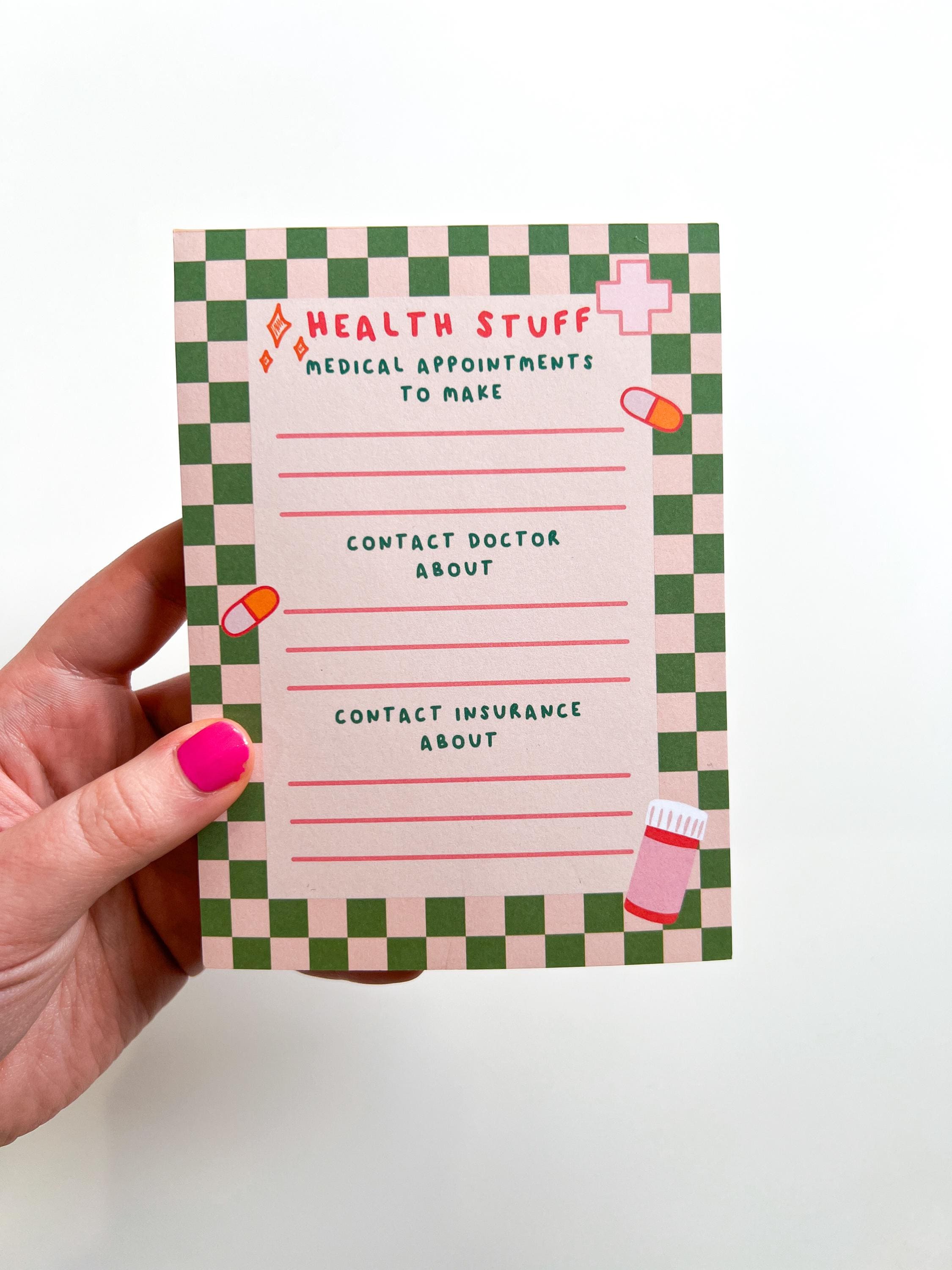 Health To Do List Notepad with beige and bright green checkered print as the border. Top of the page says, "Health Stuff" in a bright pink color. The different sections with pink lines underneath them read, "medical appointments to make, contact doctor about, and contact insurance about". Notepad is pictured being held in front of white table. 