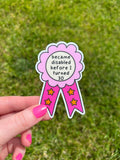 Award ribbon sticker in a light pink and dark pink shades, the middle is cream colored with the black font reading, "became disabled before I turned 30". Sticker is being held over grass. 