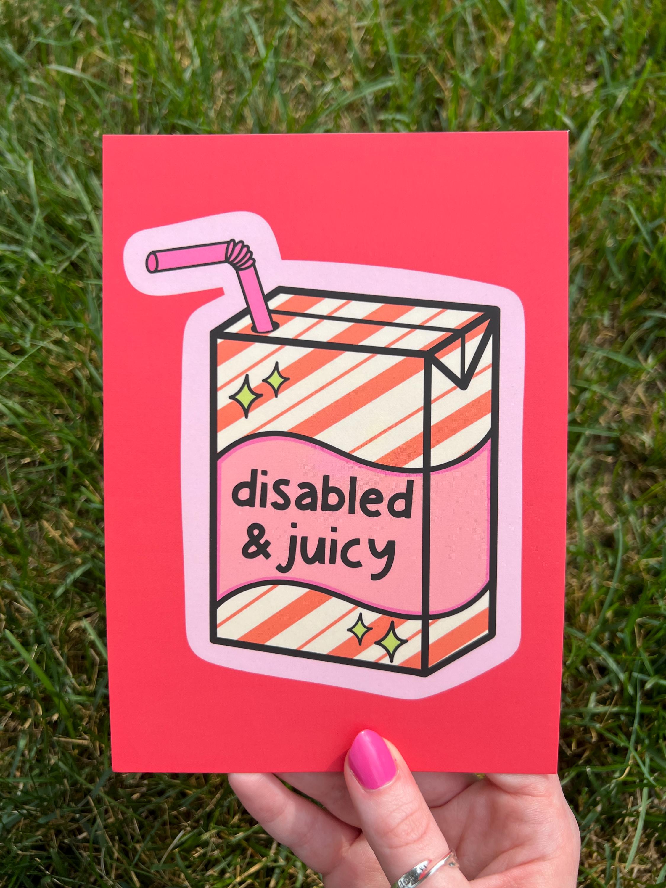 Art print with bright coral background with juice box in the center outlined in light pink. Juice box is cream with orange diagonal stripes and pink banner in the middle with yellow sparkles in either side. A pink straw is coming from the top. The black font on the juice box reads, "disabled and juicy". Print is being held over grass on a sunny day. 