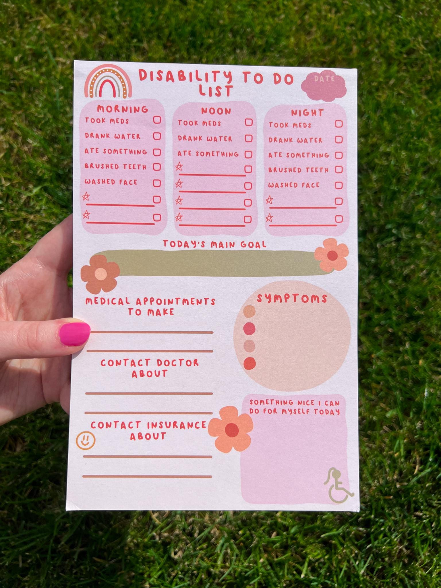 Disability To Do List Notepad with light colored sheets. Sections include: pink cloud to write the date down in, three pink boxes with red font reading "morning, noon, and night" with a checklist underneath them reading "took meds, drank water, ate something, brushed teeth, washed face" and a couple of empty spaces below to fill out yourself. There's a place to write down medical appointments to make, contact doctor about, and contact insurance about. There's a place to track symptoms. Pictured in grass.